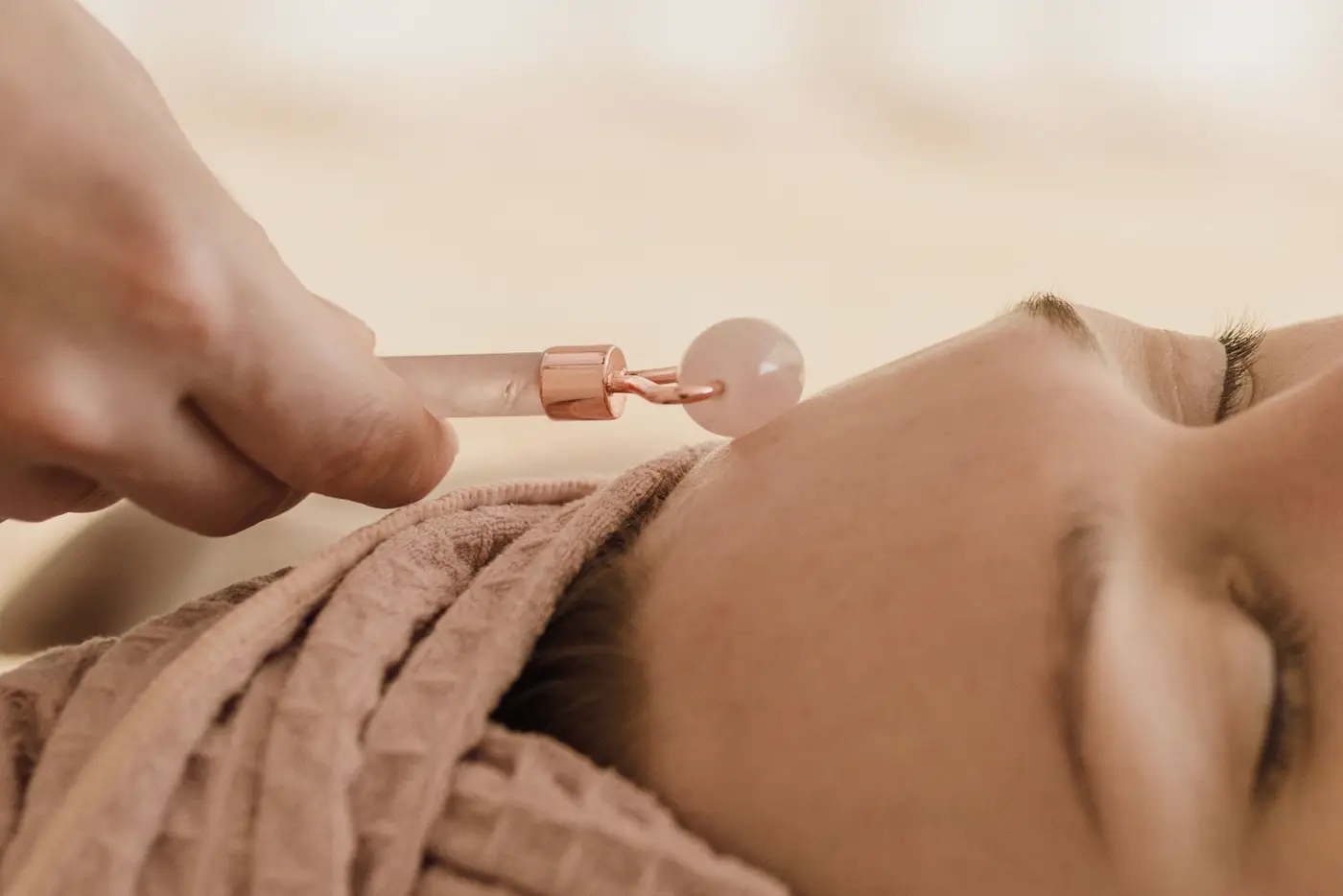 Un rouleau de massage en quartz rose glisse sur la joue, pendant un soin du visage.